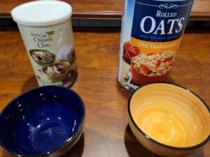 picture of two containers of oatmeal; one is steel cut, the other is rolled oats. There is a bowl in front of each oatmeal product.
